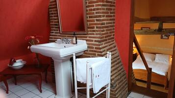 A bathroom with a white sink, a mirror, a towel rack, and a wooden bed.