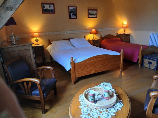 A bedroom with a wooden bed, two bedside lamps, a wooden nightstand, a chair, a small table with a tray, and framed pictures on the wall.