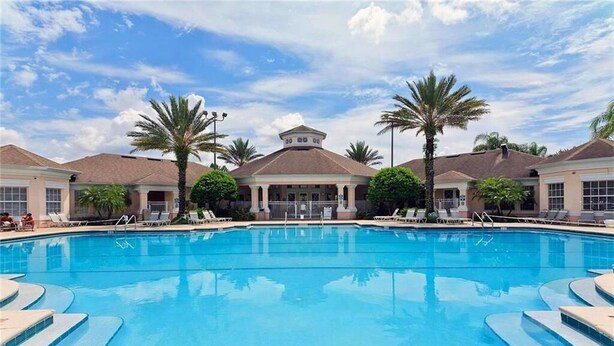 A swimming pool with lounge chairs and palm trees, surrounded by buildings with a symmetrical design. - Windsor Palms Retreat: Pool, Resort Access & Minutes to Disney (Kissimmee)