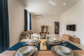 Ein Essbereich mit Tisch für vier Personen, einer Couch, einem Fernseher und einer Treppe.
