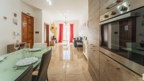 A modern kitchen with a built-in oven and a dining area with a table set for two. - Marsalforn Apartment Walk to Beach Seaside Living (Żebbuġ)