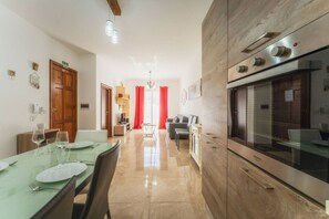 A modern kitchen with a built-in oven and a dining area with a table set for two. - Marsalforn Apartment Walk to Beach Seaside Living (Żebbuġ)