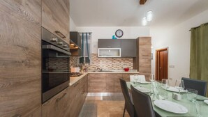 A modern kitchen with wooden cabinets, a built-in oven, and a dining area with a table set for four. - Marsalforn Apartment Walk to Beach Seaside Living (Żebbuġ)