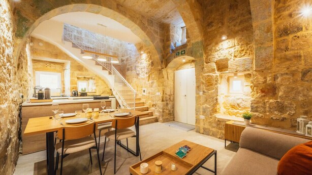 Interior de paredes de piedra con comedor, cocina y escalera.