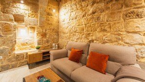 Una habitación con paredes de piedra, un sofá, cojines, una mesita de madera y una pequeña mesa con objetos decorativos.