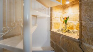 Una escalera con barandillas blancas y un muro de piedra, con una lámpara y un florero con flores.