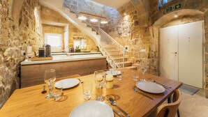 Un comedor con una mesa de madera dispuesta para cuatro, una cocina al fondo y una escalera de piedra.