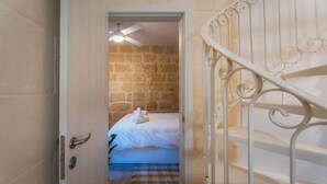 Una habitación con una cama, una puerta blanca, una escalera con barandilla blanca y un ventilador de techo.