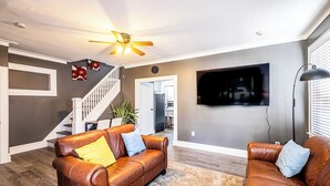 A living room with two leather sofas, a ceiling fan, a flat-screen TV, and a staircase leading to another level. - Orange Queen LLC (East Orange)