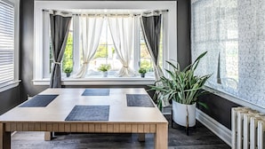 A dining area with a table, curtains, potted plants, and a patterned wall. - Orange Queen LLC (East Orange)