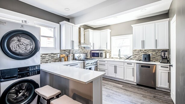 A modern kitchen with a built-in washer, a central island, and white cabinetry. - Orange Queen LLC (East Orange)