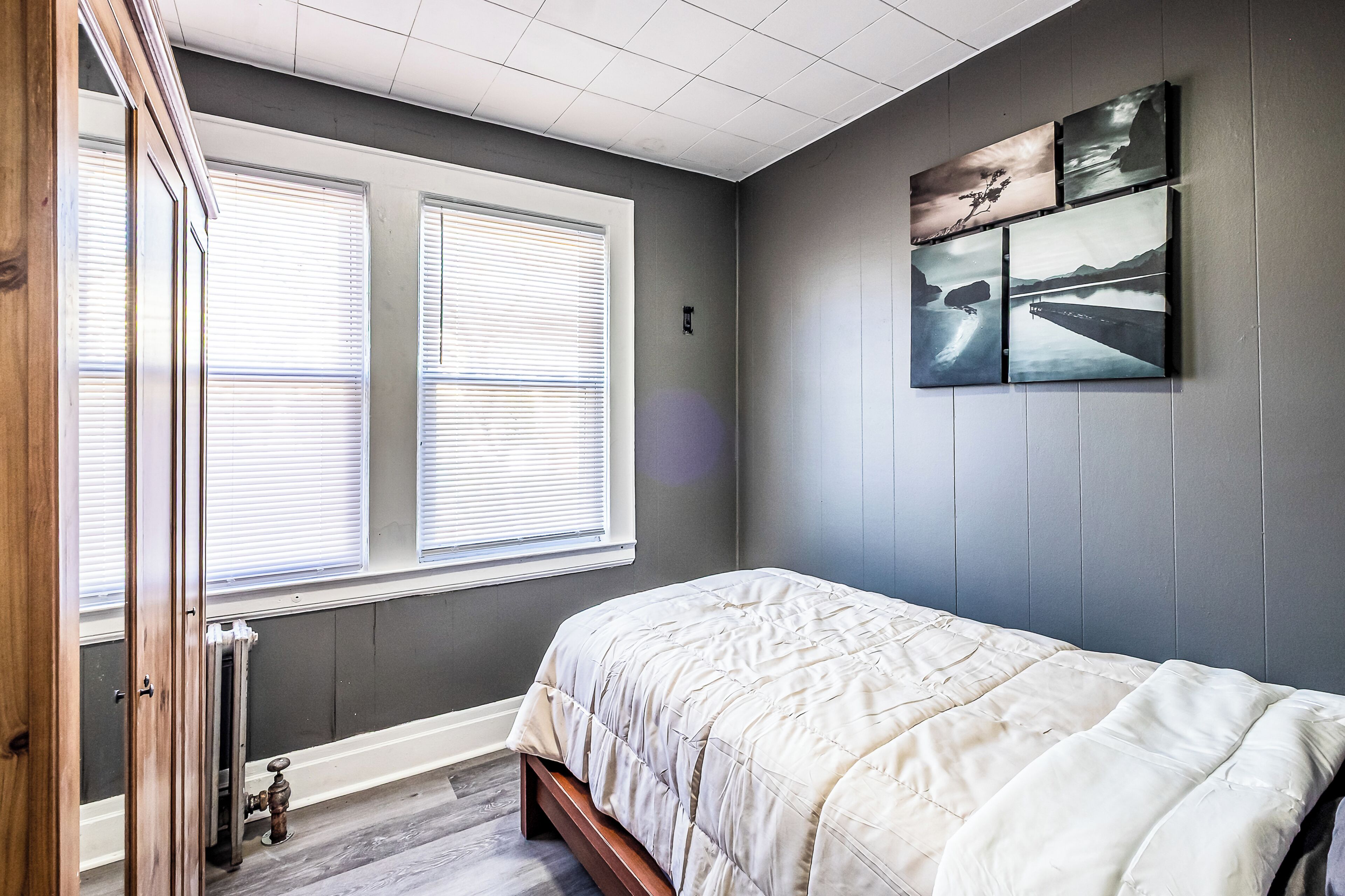 A bedroom with a bed, a radiator, a window with blinds, and wall-mounted artwork.