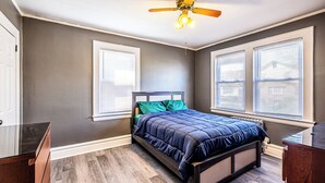 A bedroom with a bed, a ceiling fan, and two windows with blinds. - Orange Queen LLC (East Orange)