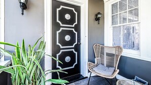 A black door with decorative glass panels, a wicker chair, and a potted plant. - Orange Queen LLC (East Orange)