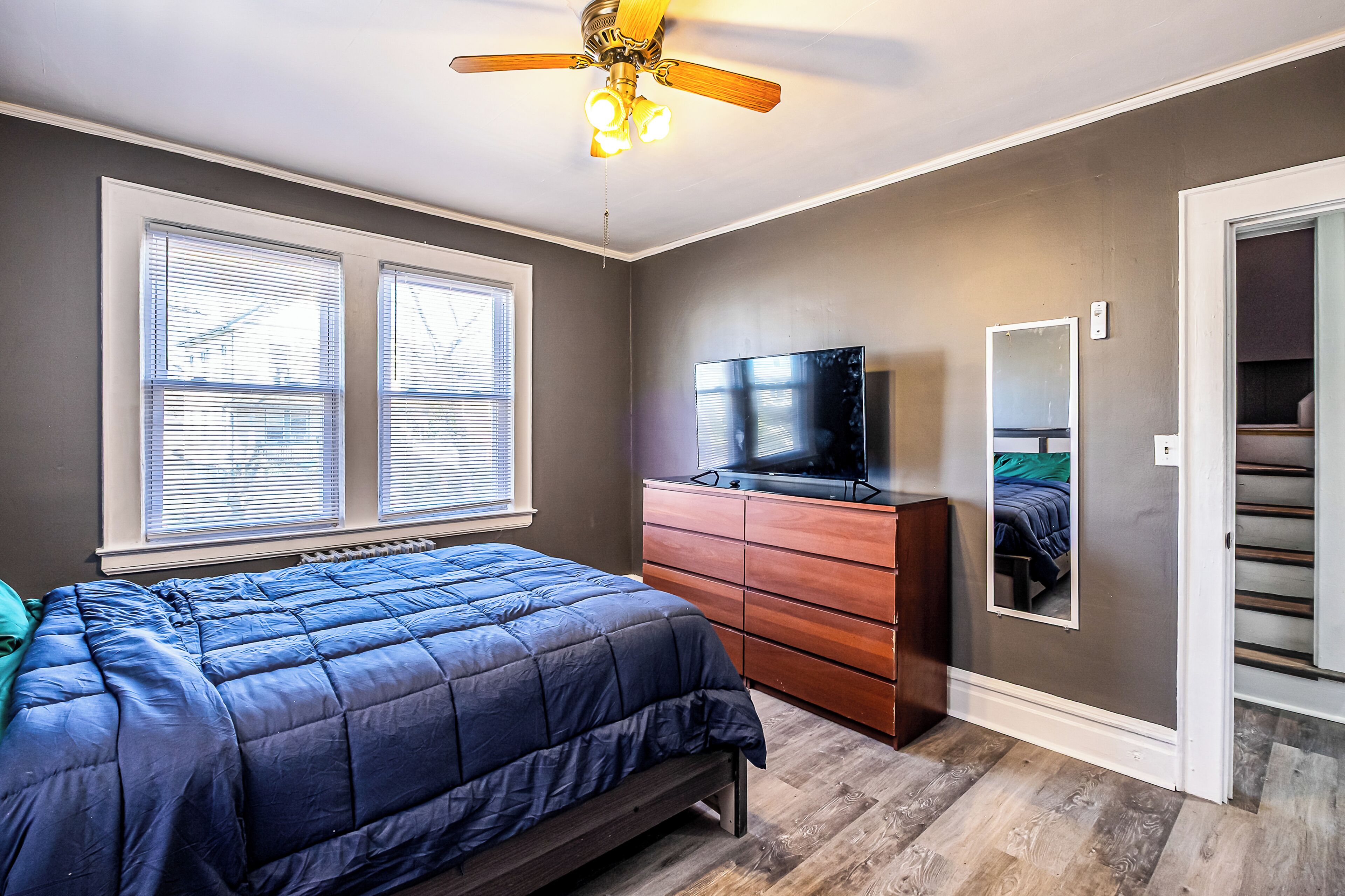 Une chambre à coucher avec un lit, une commode, une télévision et un miroir.