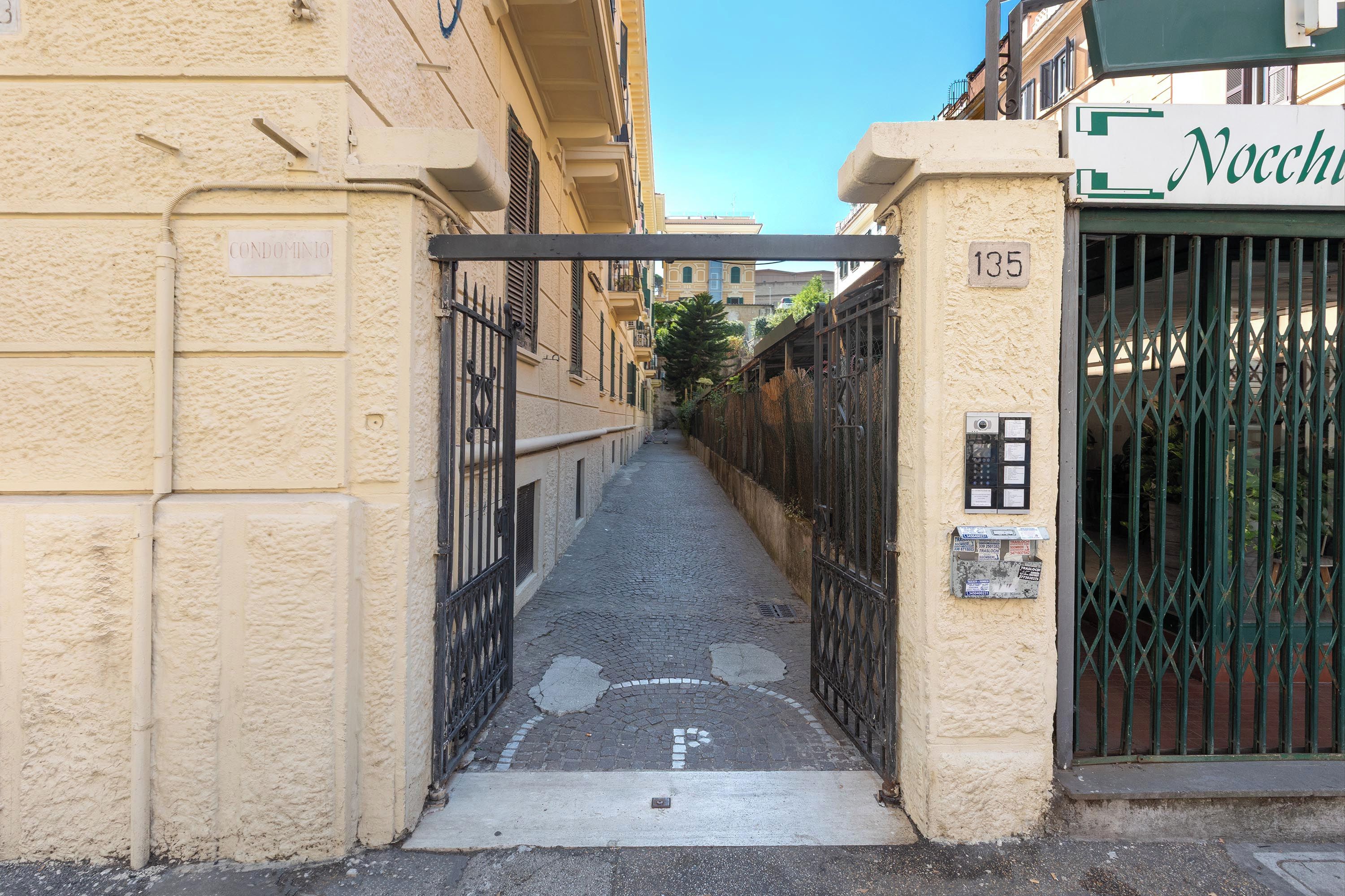 Un stretto vicolo con un cancello, una targa che indica una proprietà condominiale, e un edificio con un cancello verde con l'indicazione 'Nocchio'.