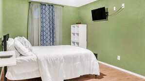 Un dormitorio con cama, televisor montado en la pared, ventilador de techo y ventana con cortinas.