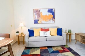 Ein Wohnzimmer mit einer Couch, einer Lampe, einem bunten Teppich und einem Gemälde an der Wand.