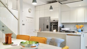 Una cucina moderna con mobili bianchi, elettrodomestici in acciaio inossidabile e un'area pranzo con tavolo e sedie in vetro.