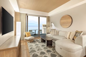 A modern hotel room with a large TV, a sofa, a coffee table, a chair, and a view of the sea. - Waikiki | Romantic Ocean Escape | Pool + Spa (Honolulu)