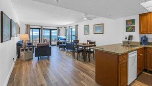 A spacious living area with a dining table, a sofa, and a kitchen area with wooden cabinets and a dishwasher. - Beachfront Getaway with Resort-Style Pool (Madeira Beach)
