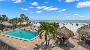 A pool area with lounge chairs, palm trees, and a beach in the background. - Beachfront Getaway with Resort-Style Pool (Madeira Beach)
