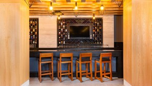 Una zona de bar con paredes de madera, una gran pantalla de televisión y cuatro taburetes de madera.