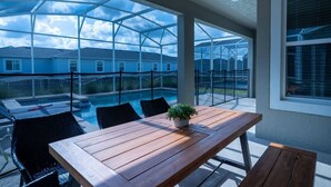 A covered patio with a wooden table, chairs, and a potted plant. - 6BR Villa w Pool & Game Room near Disney (Davenport)