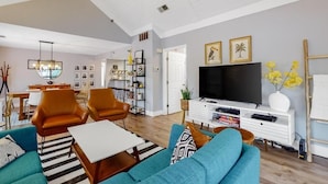 Una sala de estar con sofá, sillas, mesa de centro, televisor y estantería.