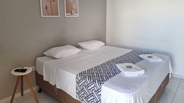 Una cama con ropa blanca, un plaid estampado y dos cuadros en la pared.
