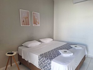 A bed with white bedding, a patterned throw, and two framed pictures on the wall.