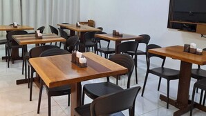 Un salón de conferencias con varias mesas y sillas, un televisor de pantalla plana montado en la pared y un ventanal con cortinas.