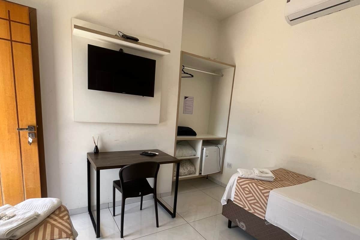 A hotel room with a bed, a desk with a chair, a television, and a wardrobe.