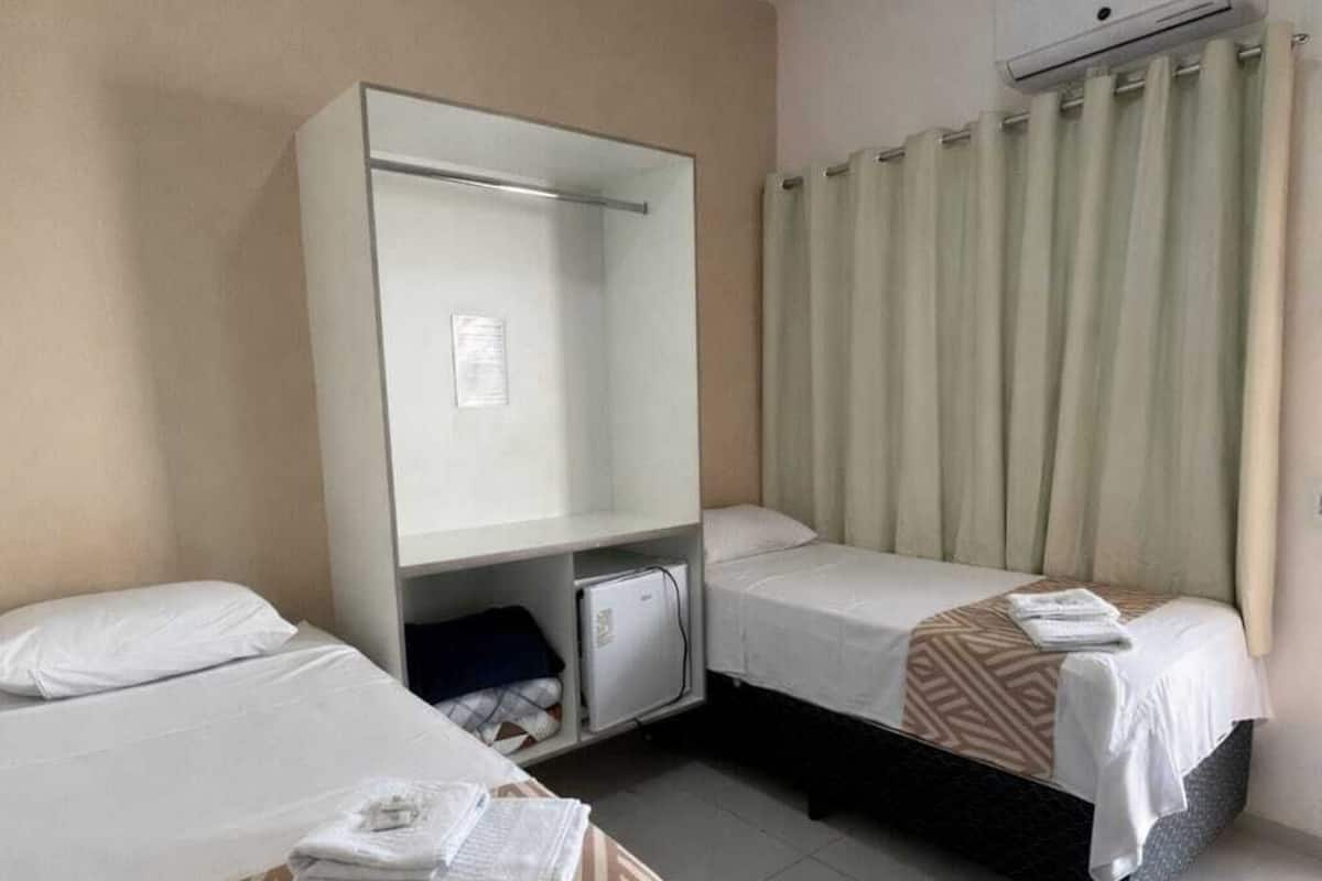 A hotel room with two beds, a wardrobe, a desk, and an air conditioning unit.