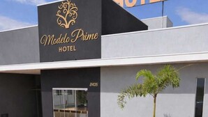 Un hotel llamado 'Madelo Prime Hotel' con una fachada moderna, una entrada de vidrio y una palmera frente a él.
