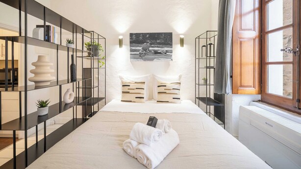 Habitación de hotel con una cama grande, una estantería metálica negra, un florero blanco y una fotografía blanco y negro en la pared.