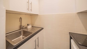 Una cocina compacta con un lavamanos de acero inoxidable, un horno empotrado y paredes de azulejos blancos.