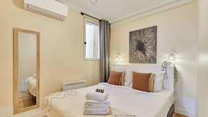 Ein Hotelzimmer mit einem Bett, einem Spiegel, einem Fenster mit Vorhängen, einer Wand-Klimaanlage und einem Wandbild.