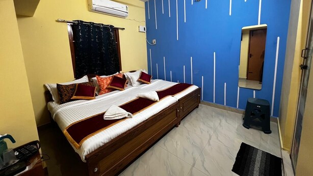 Un dormitorio con cama, ventilador de techo, ventana con cortinas, espejo y un taburete pequeño.