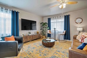 A living room with a sofa, armchair, coffee table, TV, and a ceiling fan.