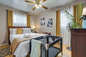 A hotel room with a bed, a desk, a chair, a ceiling fan, and a large window with curtains.