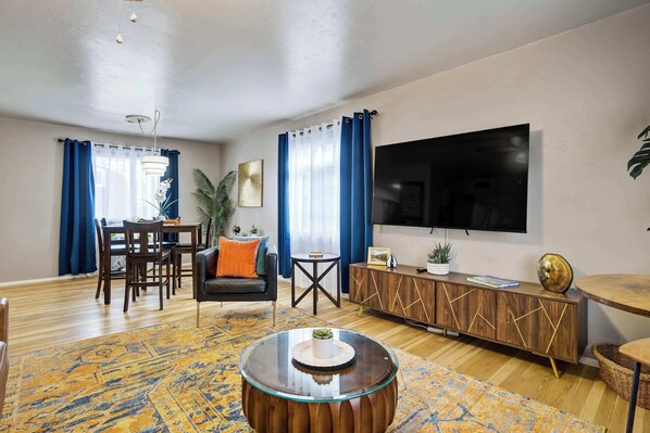 A living room with a dining area, a TV, a round coffee table, and a patterned rug.