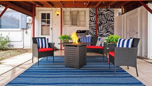 Un patio techado con una parrilla, muebles de exterior y un tapete azul a rayas.