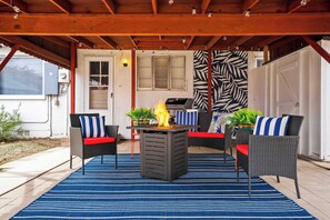 A covered patio with a grill, outdoor furniture, and a blue striped rug.
