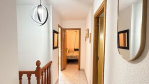 Un pasillo con una escalera de madera, una lámpara colgante y un espejo en la pared.