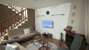 Una sala de estar moderna con sofá, sillón, mesa de centro y televisor montado en la pared.