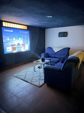 Un salon doté d’un grand écran affichant l’interface d’une application, d’un canapé bleu, d’une table basse avec une télécommande et d’un projecteur fixé au mur.