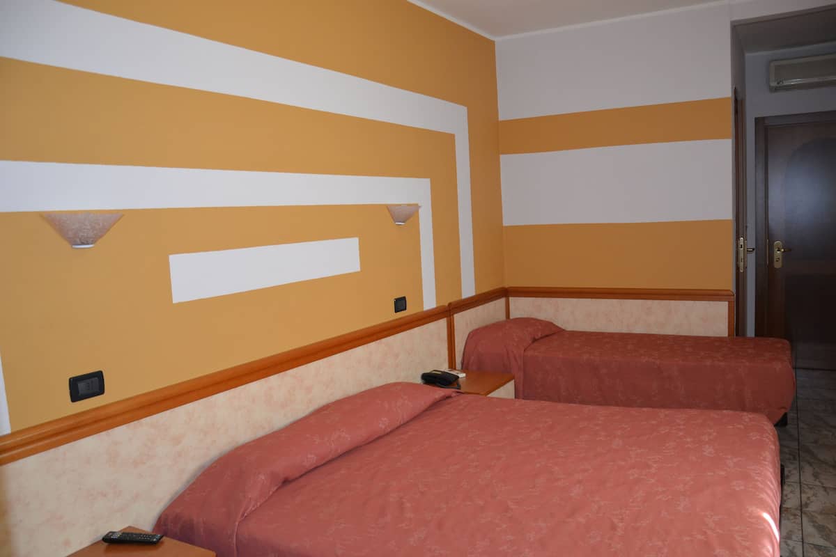 Hotellihuone, jossa on kaksi sänkyä, puinen pääty ja seinään kiinnitetty valaisin sekä ovi.