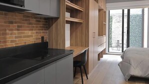 Eine moderne Küche mit schwarzem Arbeitsplatz und grauen Schränken, ein Essbereich mit Holztisch und ein Schlafzimmer mit Bett und einer Schiebeglastür zum Balkon.