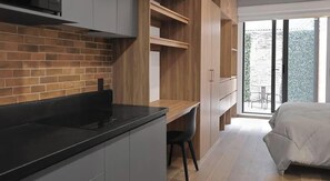 A modern kitchen with a black countertop and grey cabinets, a wooden dining area, and a bedroom with a bed and a sliding glass door to a balcony. - Colonia Americana Safe Neighborhood for World Cup (Guadalajara)